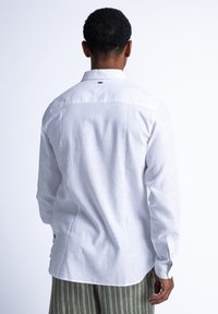 Witte lange mouwen shirt van linnen, met een gebogen onderkant, knoopmanschetten en een subtiele textuur met een rugnaaddetail.