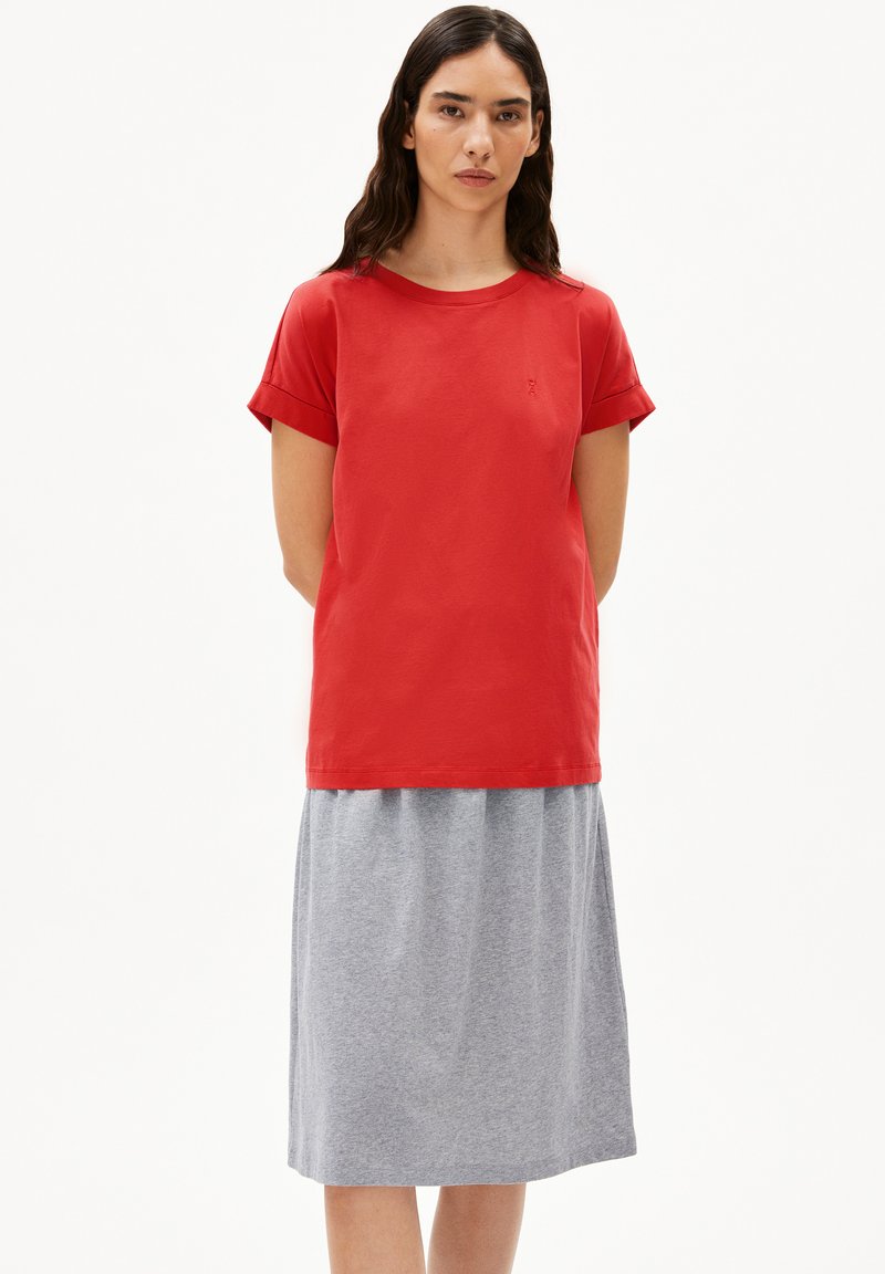 Rode katoenen T-shirt met korte opgerolde mouwen, gecombineerd met een grijze knie-lange rok. Eenvoudig ontwerp, zachte textuur en een relaxte pasvorm.