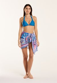 Turkizni bikini s halter vrhom. Barvit sarong s cvetnim in geometrijskimi vzorci v roza in modri barvi ovit okoli pasu.