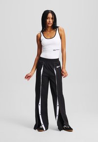 Zwarte sportbroek met witte zijkanten en drukkers; vergezeld van een witte tanktop met zwarte afwerking en logodetail.