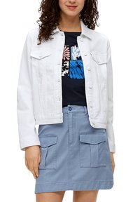 Witte denimjas met drukknopen, twee borstzakken, gedragen over een marineblauwe blouse met kleurrijke patronen, gecombineerd met een lichtblauwe rok met zakken.