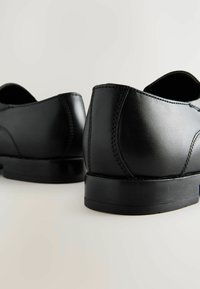 Zapatos de vestir de cuero negro con un acabado suave, forma redondeada y costuras en contraste. Presentan una suela de goma de perfil bajo para mayor durabilidad.