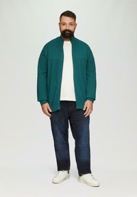 Türkise, leichte Zip-Jacke über einem weißen Shirt, kombiniert mit dunkelblauen Jeans und weißen Sneakers. Einfaches Design, lockere Passform, minimale Details.