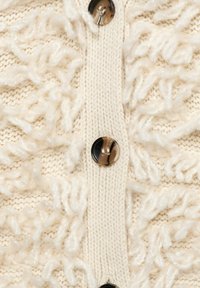 Crème kleurige gebreide cardigan met een patroon van gelooide textuur garen en schildpaddecoratie knopen aan de voorkant.