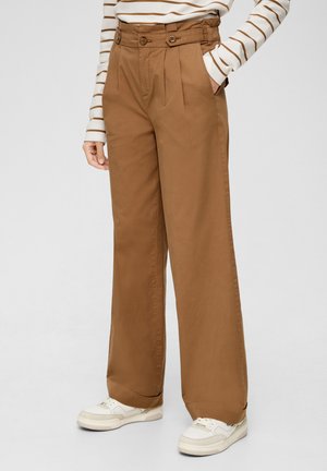 Bruine wijde pantalons met voorkruisen, hoge taille, dubbele knoopsluiting en zijzakken, gecombineerd met witte sneakers.