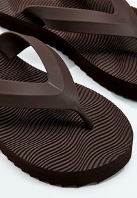 Dark brown flip-flops with textured, wavy footbed patterns and wide Y-shaped straps, on a white background.