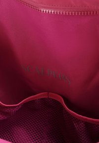 Interior de tela burdeos con un logo "SCALPERS" en gris, con un bolsillo de malla en la parte inferior y un acabado suave. Cierre con cremallera en la parte superior.