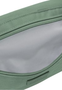 Zelený látkový sáček s texturovaným povrchem, zipovým zavíráním a hladkým, světlým vnitřkem. Na boku se nachází brandingová nálepka.