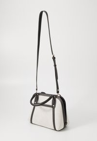 Sac à main en tissu gris clair avec des accents en cuir noir, poignées doubles et bandoulière réglable. Présente des coutures contrastées et une forme structurée.