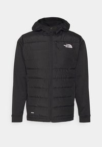 Sort isoleret jakke med lynlås foran, hætte og quiltet design på torsoen. Har The North Face-logoet på brystet.