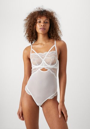 Bodysuit blanc en dentelle avec tissu transparent, bordure en dentelle florale, bretelles réglables et un design découpé à la taille.