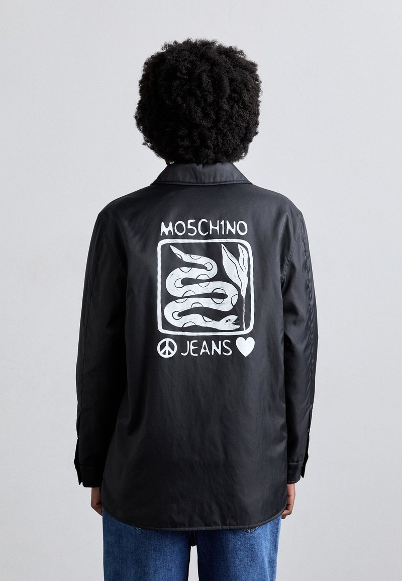 Zwarte shirt met een zichtbare witte graphic van slangen, tekst "MOSCHINO JEANS" en een vredessymbool op de achterkant. Lange mouwen, relaxed fit.