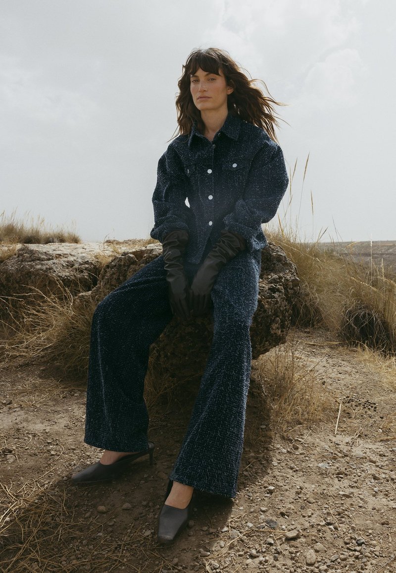 Navy textured fabric outfit with a button-up shirt and wide-leg pants, paired with brown gloves and dark heeled mules.