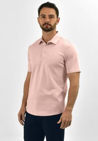 Lichtroze polo shirt met een kraag, korte mouwen en drie knopen. Heeft een subtiele logo op de linkerkant van de borst. Gladde textuur, casual ontwerp.