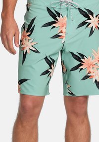 Mätovo zelené plavky s kvetinovým vzorom s broskyňovými kvetmi a čiernymi listami, vyrobené z ľahkej, rýchloschnúcej tkaniny.