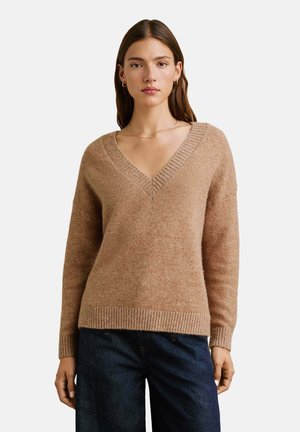 Beige v-halstrui van een zachte textuur, met geribbelde zoom en manchetten. Gepaard met donkerdenim jeans.