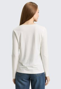 Wit shirt met lange mouwen van zachte, geribbelde stof met een ronde hals en een getailleerd model, gecombineerd met blauwe spijkerbroek.