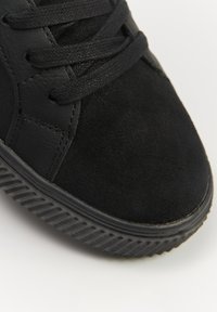 Czarne sneakersy z połączenia skórzanych i zamszowych materiałów, o okrągłym nosku, płaskiej gumowej podeszwie z teksturowanym gripem oraz czarnymi sznurówkami.