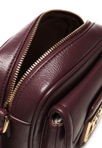 Borsa in pelle viola scuro con zip dorata parzialmente aperta, che mostra l'interno in tessuto scuro e il hardware dorato sulla tasca laterale.
