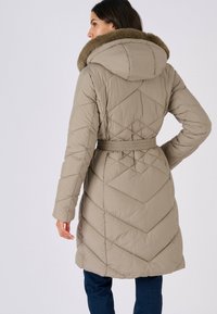 Beige, gewatteerde donzen jas met een grote capuchon gevoerd met bont, een ceintuur in de taille en een chevronpatroon op de achterkant, weergegeven vanaf de linkerkant.