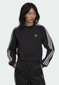 Svart kortärmad sweatshirt med ribbad halsringning, vita tre-randsdetaljer på ärmarna och liten broderad adidas-logga på bröstet.