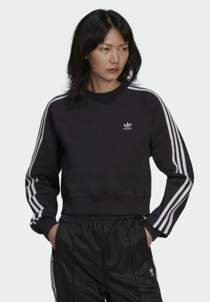 Felpa nera cropped con collo a coste, dettagli a tre strisce bianche sulle maniche e piccolo logo ricamato adidas sul petto.