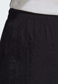 Svarta byxor med en texturerad tyg, elastisk midja och en ficka på baksidan. Materialet verkar lätt och skrynkligt.