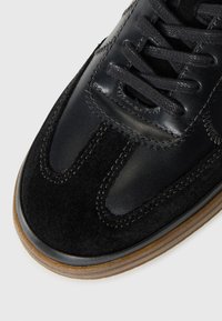 Melnas kedas ar gludas ādas un zamšādas faktūru kombināciju, ar gumijas zoli un melniem šņorēm. Izteikts šuvju akcentu dizains.