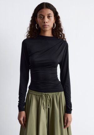 Schwarzes Langarmoberteil mit hohem Kragen und gerafftem Textur, kombiniert mit einem schwingenden olivgrünen Rock mit elastischem Bund.