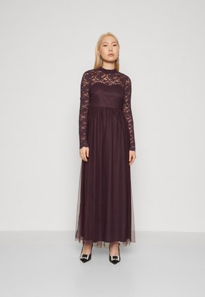 Maxi dress in dark purple with long lace sleeves, a fitted bodice, and a flowing tulle skirt. Paired with black pointed-toe shoes.
