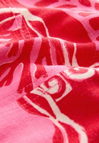 Tissu en coton aux nuances de rose et de rouge présentant un motif abstrait moderne avec des formes et des lignes tourbillonnantes, mettant en valeur une finition texturée.