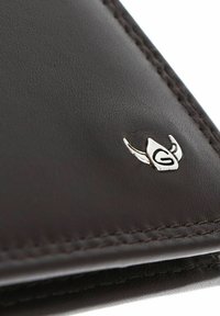 Gros plan sur le coin d'un portefeuille en cuir brun foncé avec une couture détaillée et un petit emblème argenté en forme de casque de viking avec la lettre G.