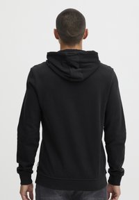Sudadera de algodón negra con un gran bolsillo trasero, puños y dobladillo acanalados. Presenta un corte holgado y capucha ajustable con cordón.
