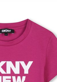 Camiseta de algodón fucsia con cuello redondo y mangas cortas, con un gran texto blanco que dice "DKNY NEW" en el frente.