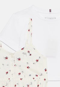 Άσπρο κοντομάνικο μπλουζάκι φορεμένο κάτω από φόρεμα εκρού με κόκκινο λουλουδάτο σχέδιο, κουμπιά εμπρός και λεπτές τιράντες στους ώμους.