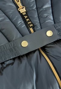Chaqueta acolchada en azul marino oscuro con un acabado brillante. Presenta un cierre dorado, grandes broches dorados y una cinturilla elástica texturizada para un ajuste adecuado.
