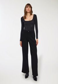 Body a maniche lunghe nera con motivo a pois bianchi, abbinato a pantaloni neri a gamba larga e stivali alla caviglia con tacco a blocco. Finitura in tessuto liscia.