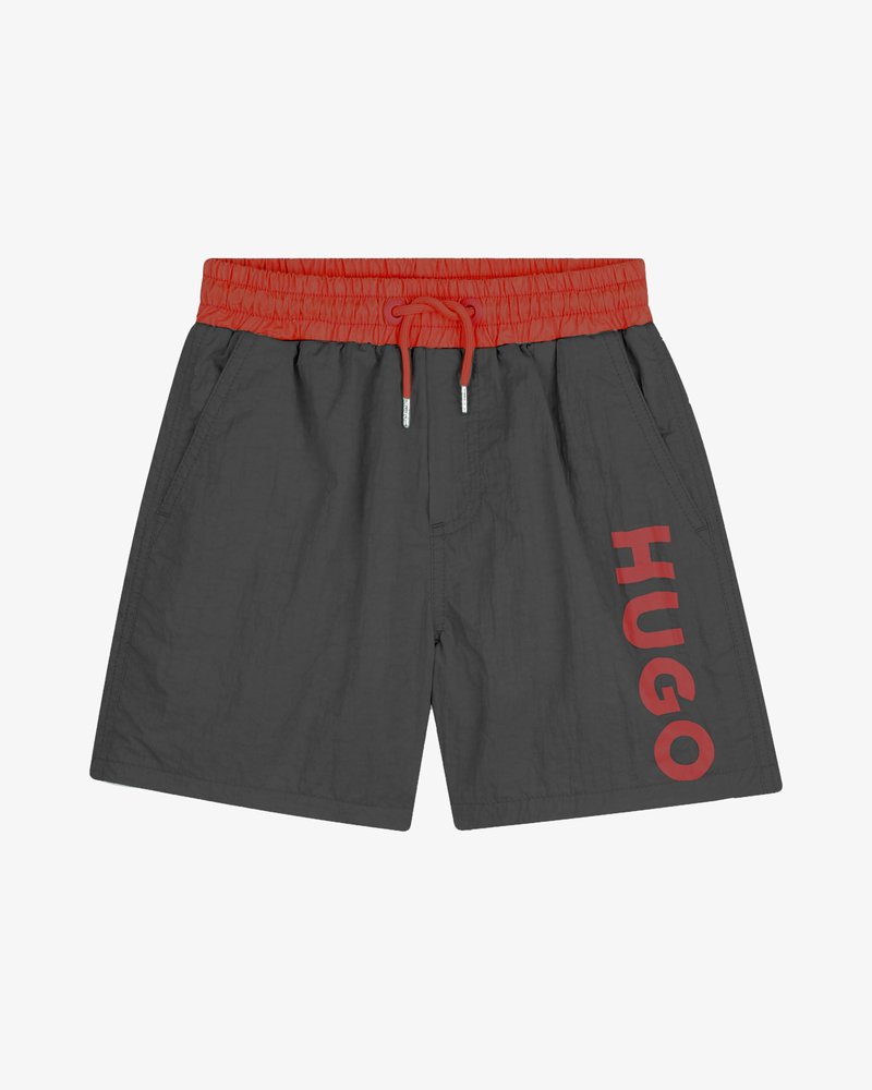 Shorts gris avec une ceinture élastique rouge, dotés de poches latérales et du mot « HUGO » imprimé en rouge vif sur la jambe gauche.