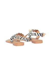 Sandali piatti con suola marrone. Le cinghie presentano un motivo zigzag bianco e nero, dotate di una fibbia e di dettagli decorativi in frange.