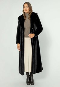 Černý kabát z umělé kožešiny s plyšovou texturou, s klopovým límcem, dvojitým zapínáním a dlouhými rukávy, kombinovaný s béžovou sukní.