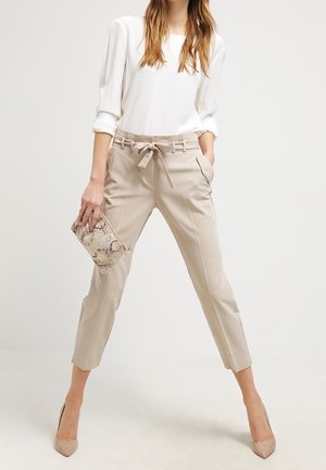 Beige skräddarsydda byxor med knytband i midjan, smalnande ben och sidofickor, kombinerade med en vit topp och en clutch med ormskinnsmönster.