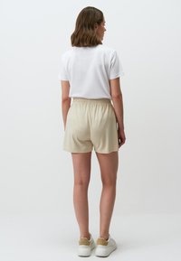 Crème kleurige shorts met een elastische tailleband en twee zijzakken, gecombineerd met een fitting wit t-shirt en witte sneakers.