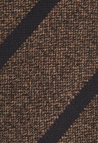 Kohandatud kudum, mis on pruun ja must, diagonaalsete triipudega. Materjal tundub jäme ja erineva kiudude paksusega.