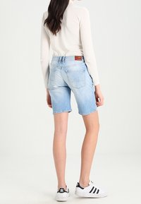 Shorts de mezclilla azul claro, de longitud hasta la rodilla, con un bajo deshilachado. Se ven los bolsillos traseros. Combinados con zapatillas blancas con rayas negras.