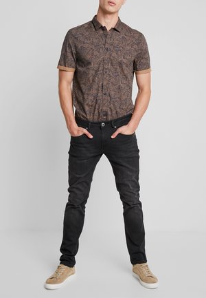 Korte mouwen, bruin paisley-patroon shirt met een kraag, gecombineerd met zwarte jeans en beige sneakers. Glad materiaal met een aansluitend ontwerp.
