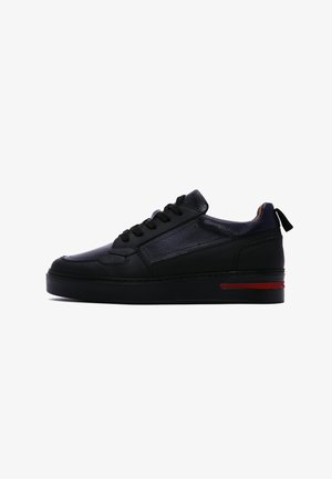 Schwarze Sneaker mit einem glatten Lederoberteil, runder Zehenpartie und einer dicken Sohle mit roten Akzenten. Auch Schnürsenkel und eine Schlaufe an der Rückseite sind vorhanden.
