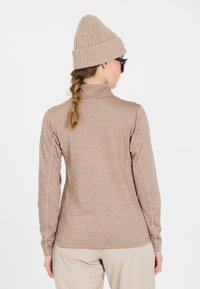 Langærmet, lysebrun, tekstureret bluse med høj krave. Har sidesømme og er parret med en strikket beige hue.