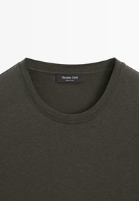 Olivgrünes T-Shirt mit Rundhalsausschnitt aus weichem, glattem Stoff. Verfügt über ein Etikett mit der Marke "Massimo Dutti" oberhalb des Nackenbereichs.