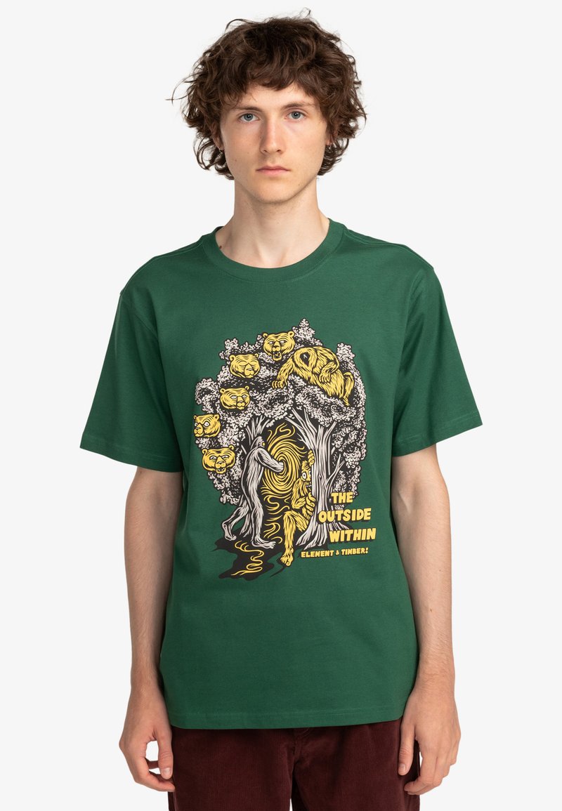 Camiseta de algodón verde con una ilustración gráfica de árboles y animales en amarillo y negro. Cuello redondo, mangas cortas, corte relajado.