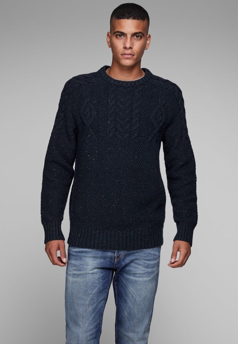 Marineblauwe gebreide trui met een gestructureerd patroon en geribbelde zoom. Bevat kabelgebreide details, gecombineerd met blauwe spijkerbroek.